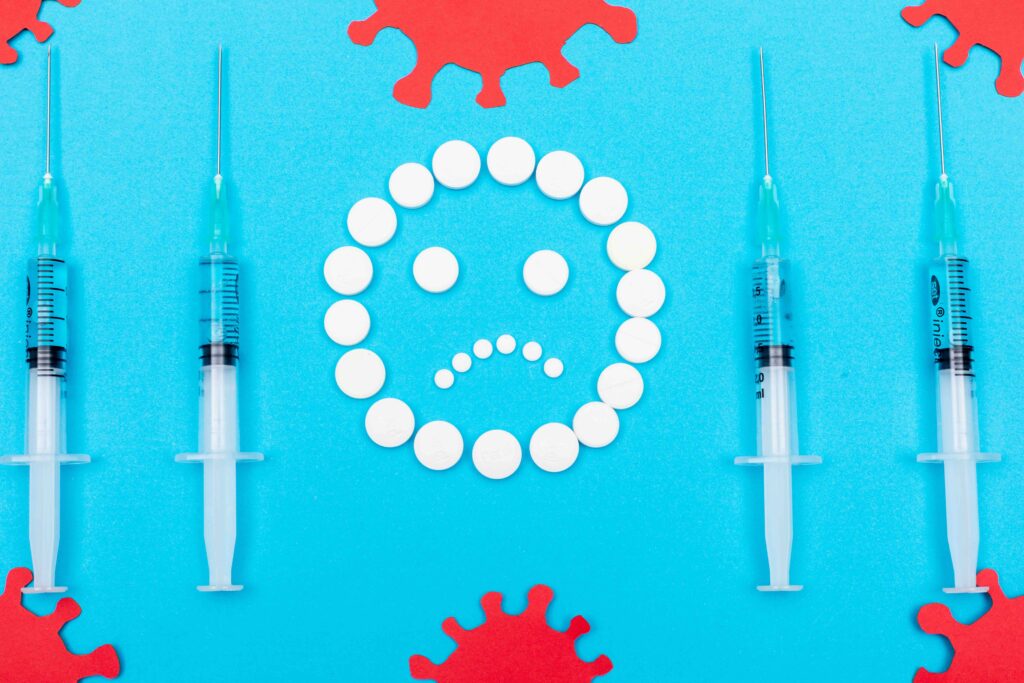 Sad face made of white pills surrounded by syringes and virus symbols, representing the emotional and medical burden of chronic disease.